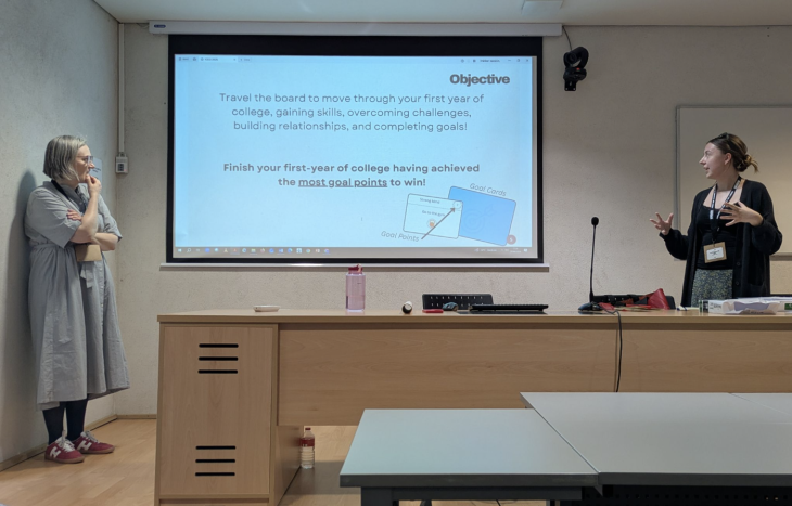 Two presenters stand at the front of a classroom discussing a slide about college readiness while addressing an audience.